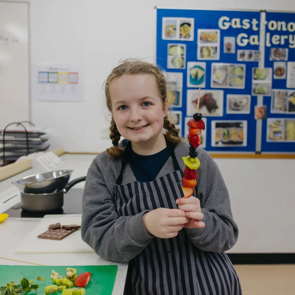 Young girl from Bridgeway School in a classroom holding up a fruit stick