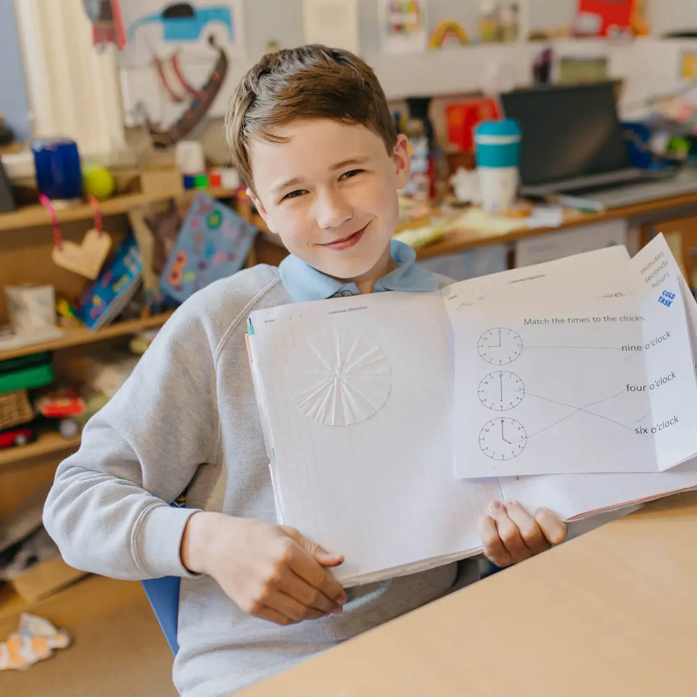 Young boy from Cedar House School sat at his desk showing off his class workbook