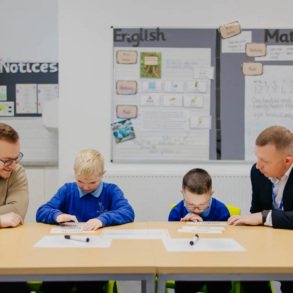 Two pupils and two members of staff sat at desks in a classroom learning