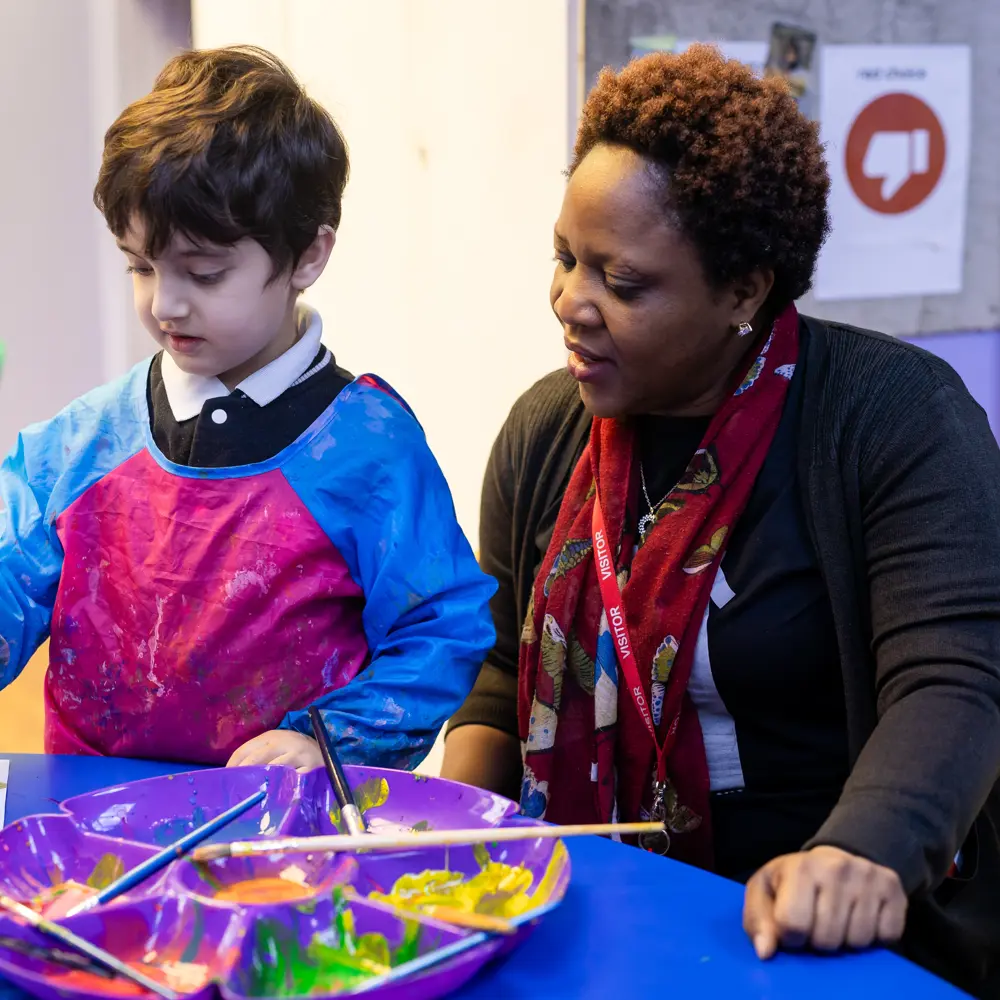 A young boy at Lavender Lodge School painting with a member of staff