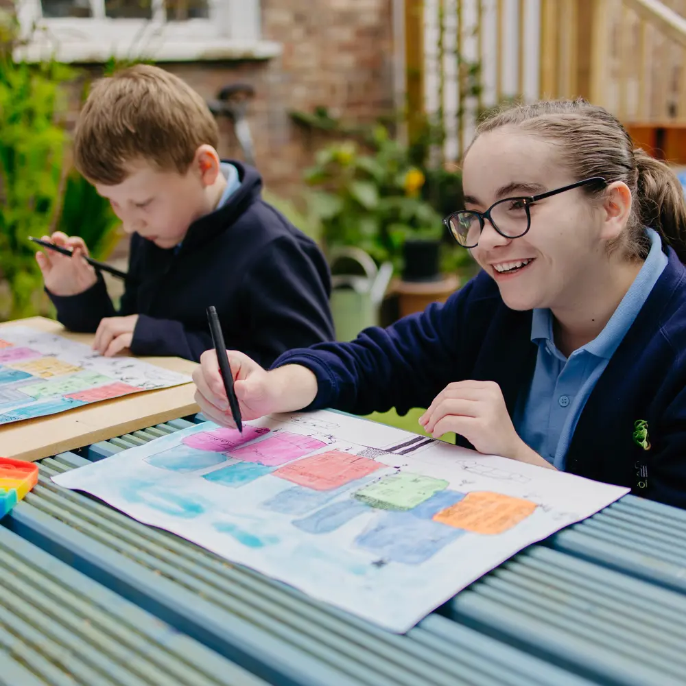 Girl and boy from Pontville School sat outside painting on a bench