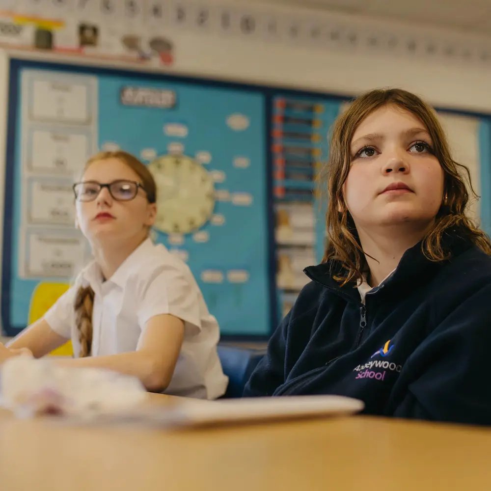 2 girls sat at a desk in a classroom focusing on their lesson at Abbeywood School