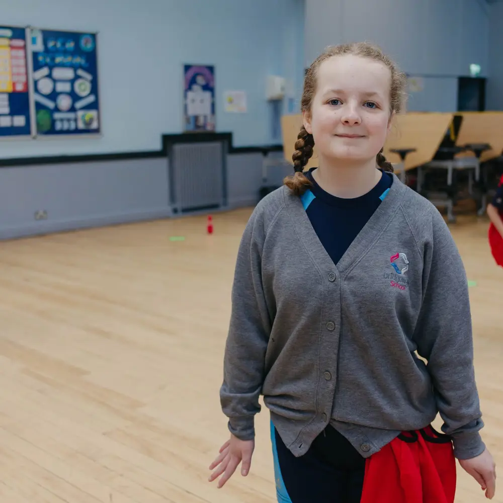 A young girl in PE kit standing in a sports hall