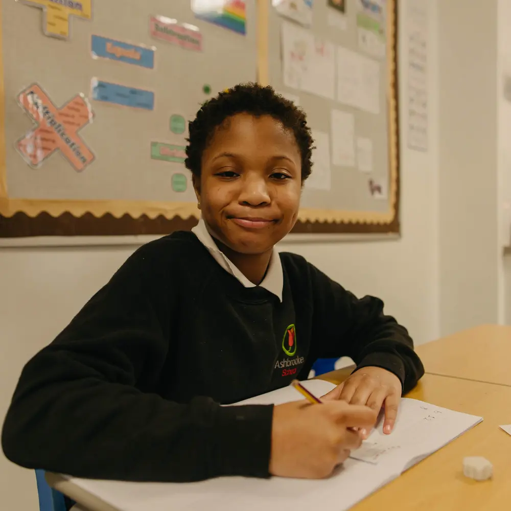 A young boy at Ashbrooke School sitting at a desk doing his school work smiling at the camera