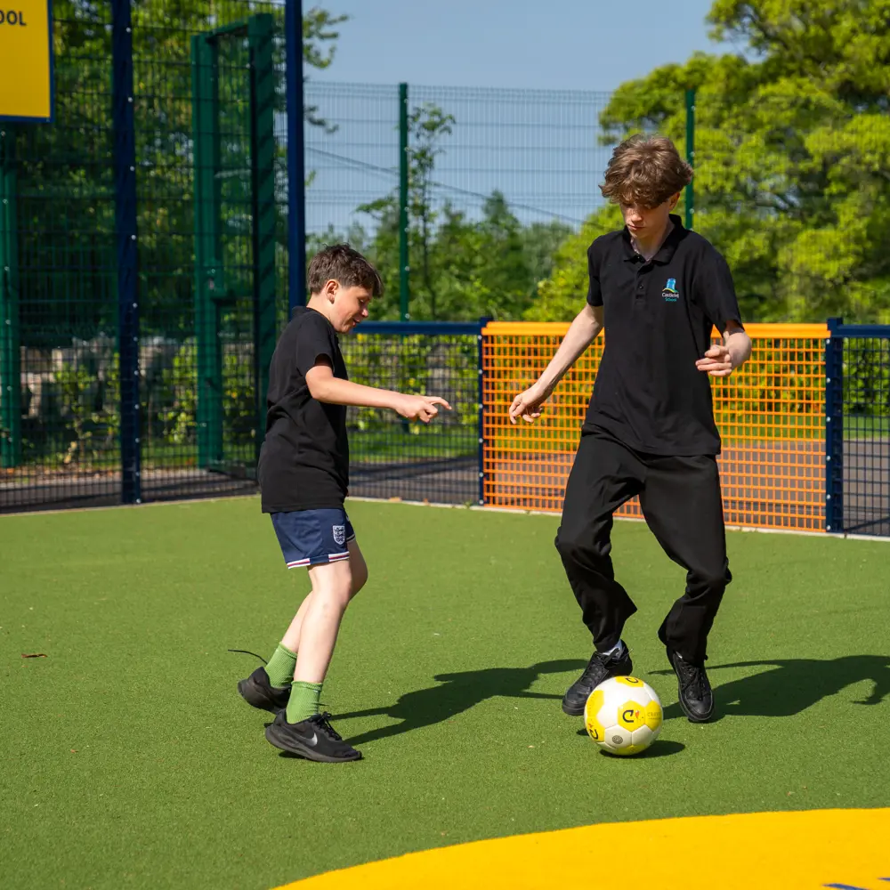 Two boys from Castlefell School playing football on the Cruyff Court in the sun