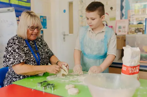 A young boy at Hall Cliffe Primary School baking with a member of staff