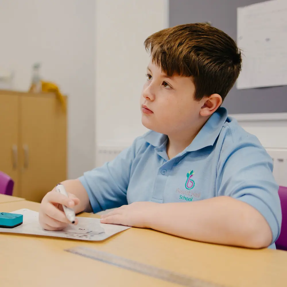 Young boy with brown hair from Bescot Hall School sat at desk doing work