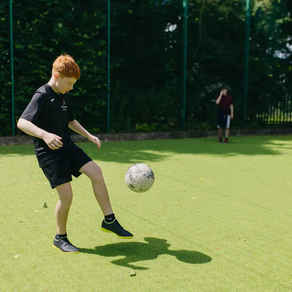 A young boy with red hair playing football outside at Abbeywood School on a sports court