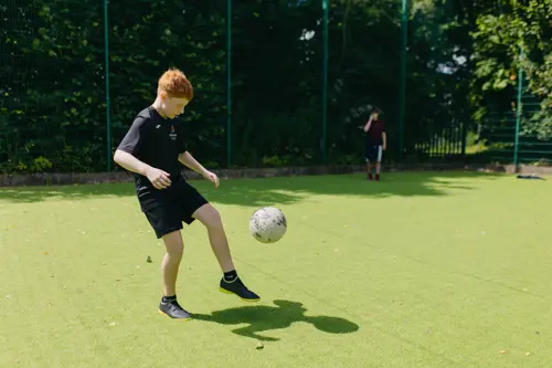 A young boy with red hair playing football outside at Abbeywood School on a sports court