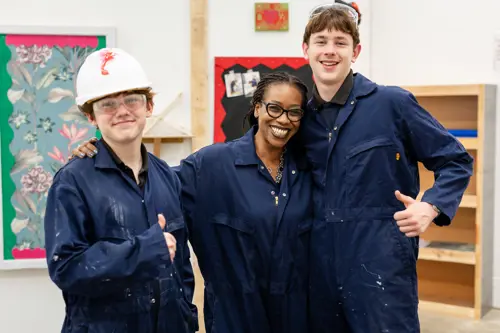 Two pupils from Avon Park School with a staff member, smiling, wearing overalls