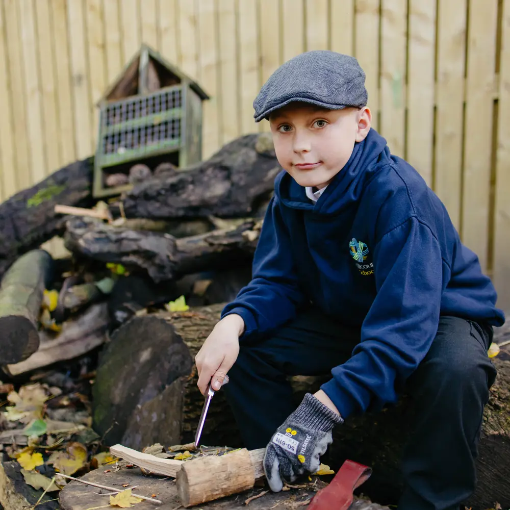 A young boy from Millcourt School crouching down in the forest school starting a fire