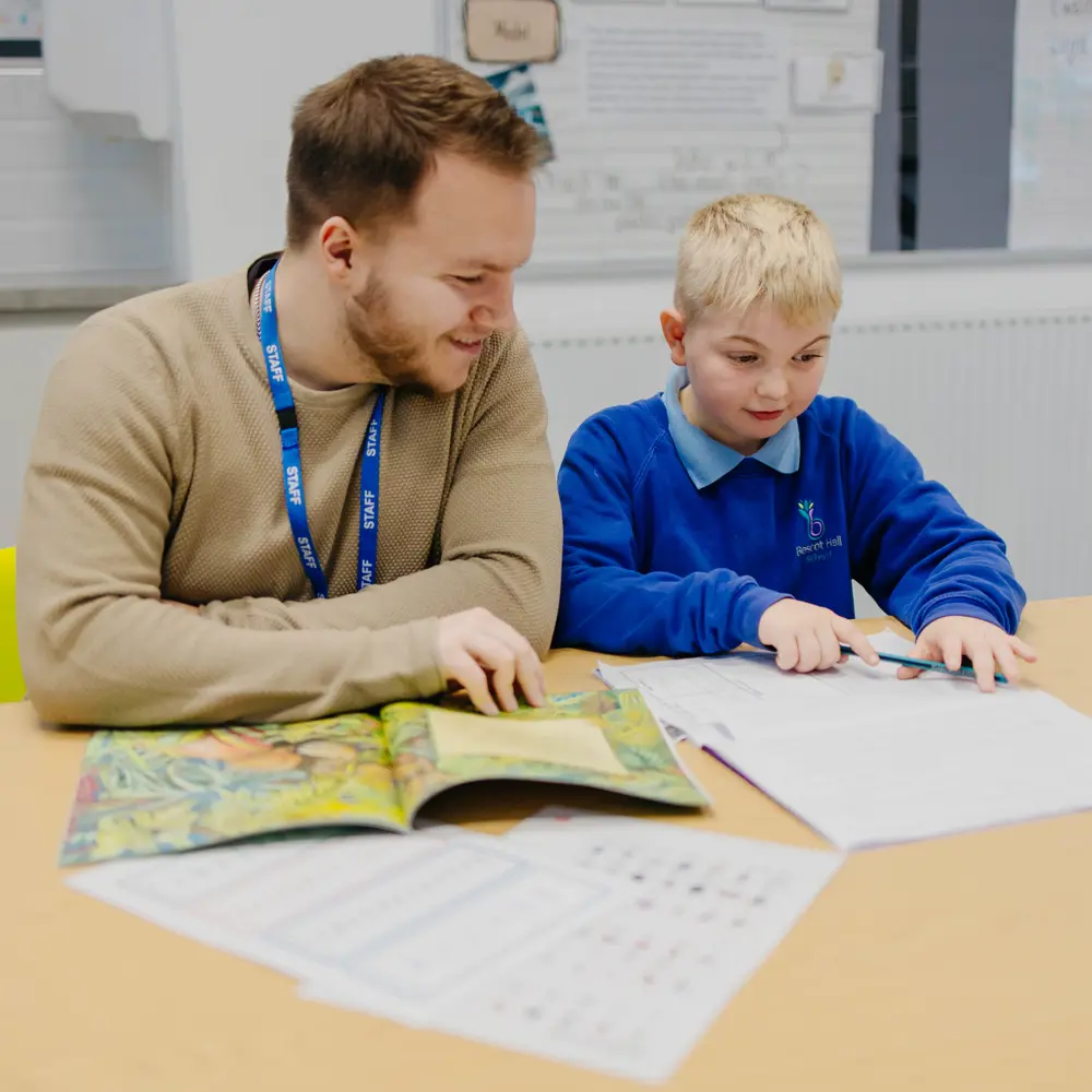 Young boy and male teacher from Bescot Hall School sat at a desk doing school work