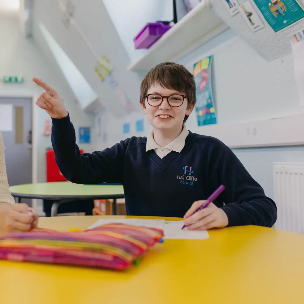 A young boy at Hall Cliffe School pointing at a teacher whilst doing his work