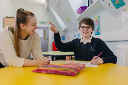 A young boy at Hall Cliffe School pointing at a teacher whilst doing his work