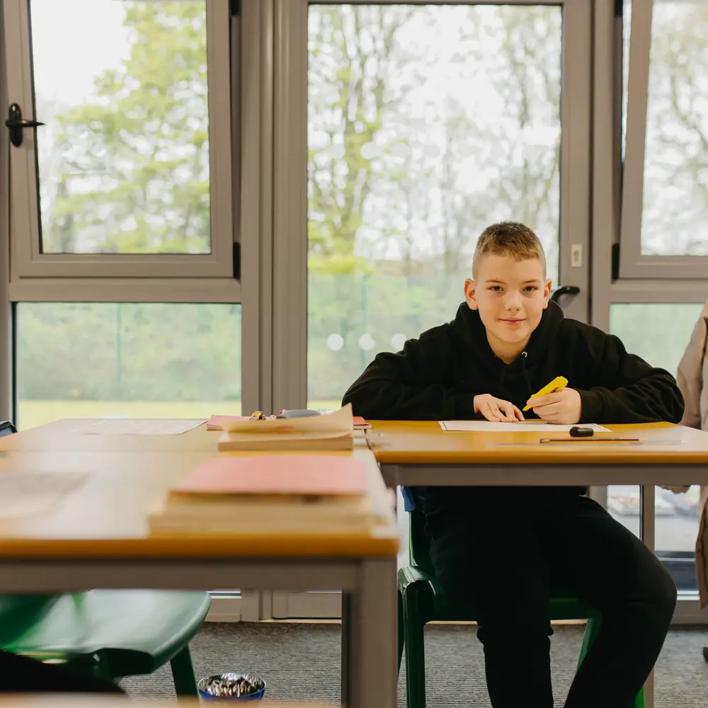 2 boys sat at their desks using yellow highlighters to complete their classwork