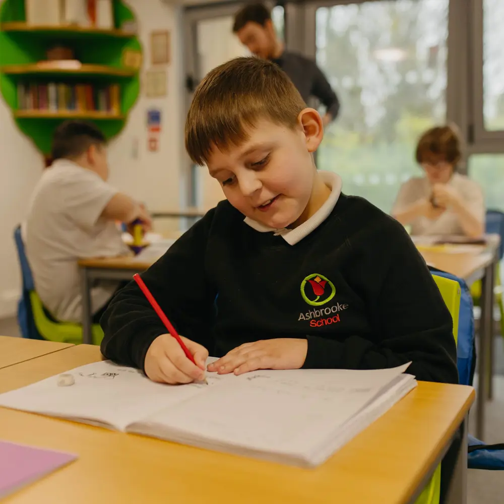 Young boy sat at his desk completing classwork in a classroom at Ashbrooke School