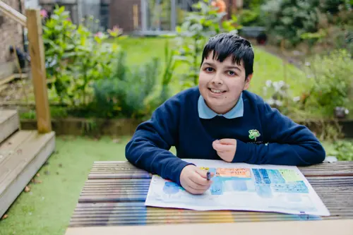 Young boy from Pontville School sat in school gardens colouring at a bench