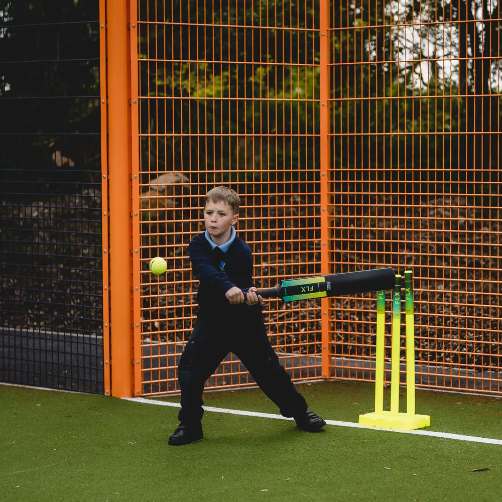 A young boy at Castlefell School playing cricket on the Cruyff court in his school uniform