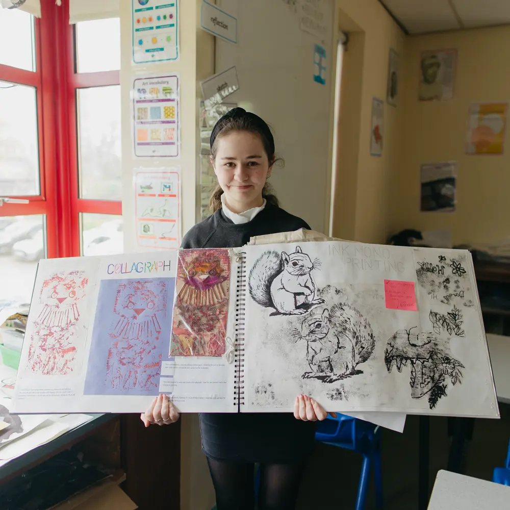 Young girl showing her artwork in a classroom at Ashbrooke School