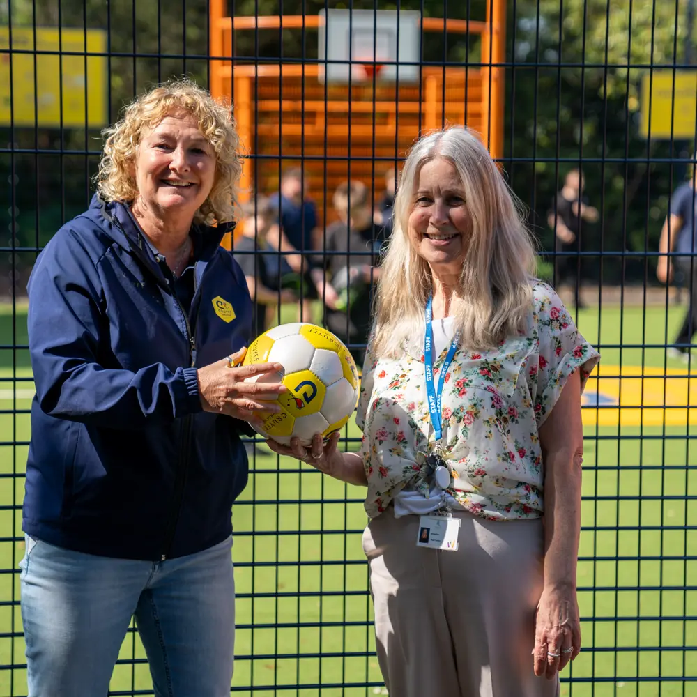 Two staff members at Castlefell School holding a football on the Cruyff Court