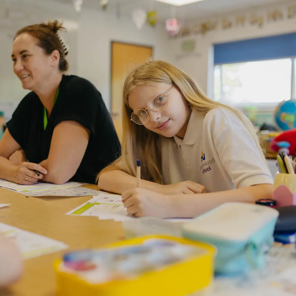 Blonde-haired girl sat at a table with a staff member at Abbeywood School