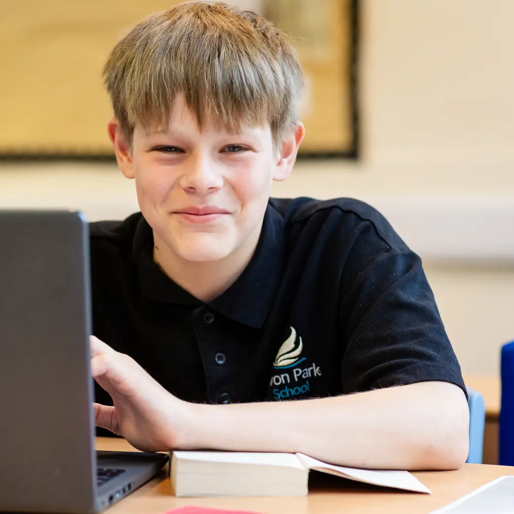Smiling boy sat at a desk with laptop at Avon Park School