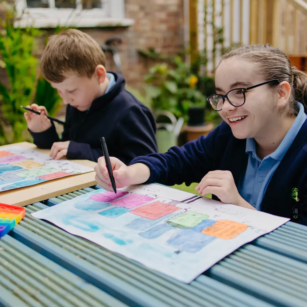 Girl and boy from Pontville School sat outside painting on a bench