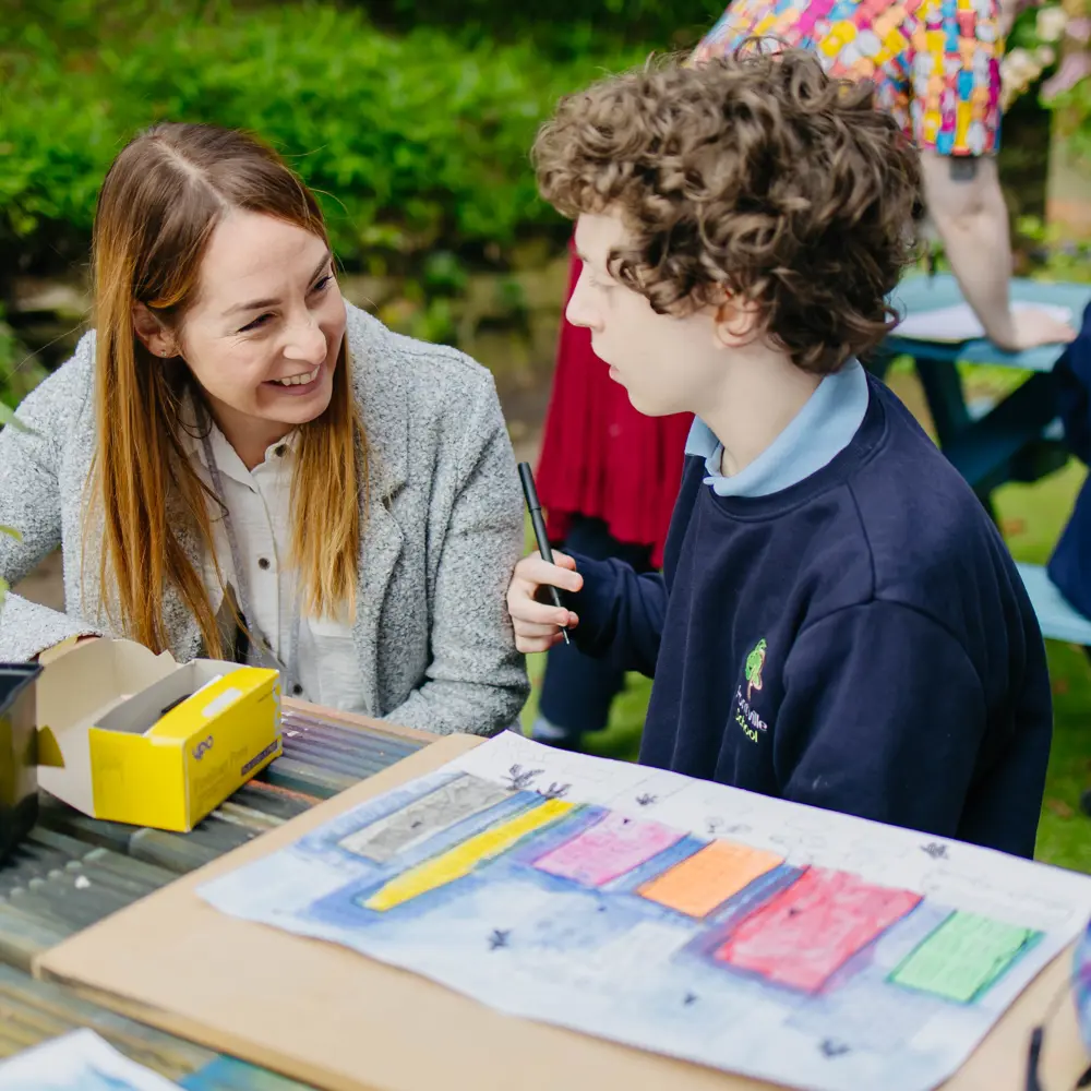 A young boy at Pontville School drawing outside on a bench with a teacher