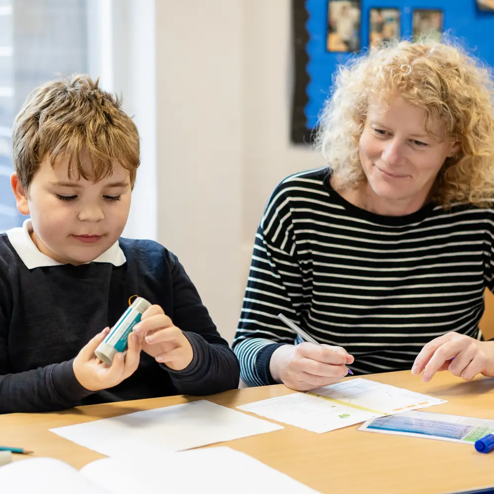 A young boy with blond hair at Queensmead House School working with a member of staff