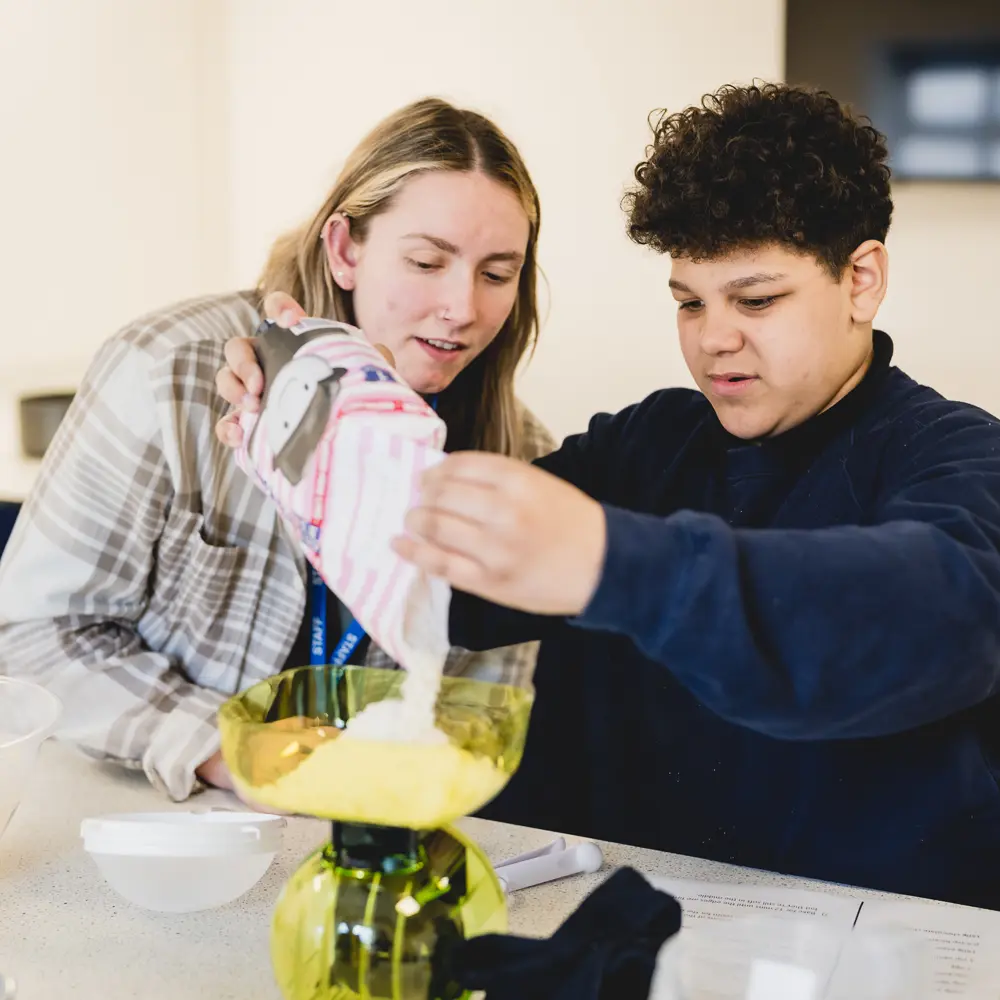 Boy from Castlefell School working with teacher to weigh out flour onto a scale