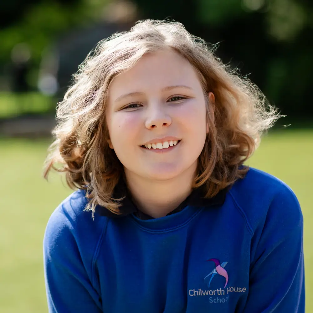 Young child from Chilworth House School with blonde curly hair sat outside smiling into camera