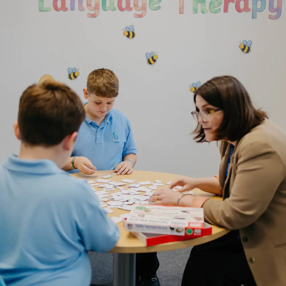 Two pupils sat at a table with a teacher at Bescot Hall school playing a card game