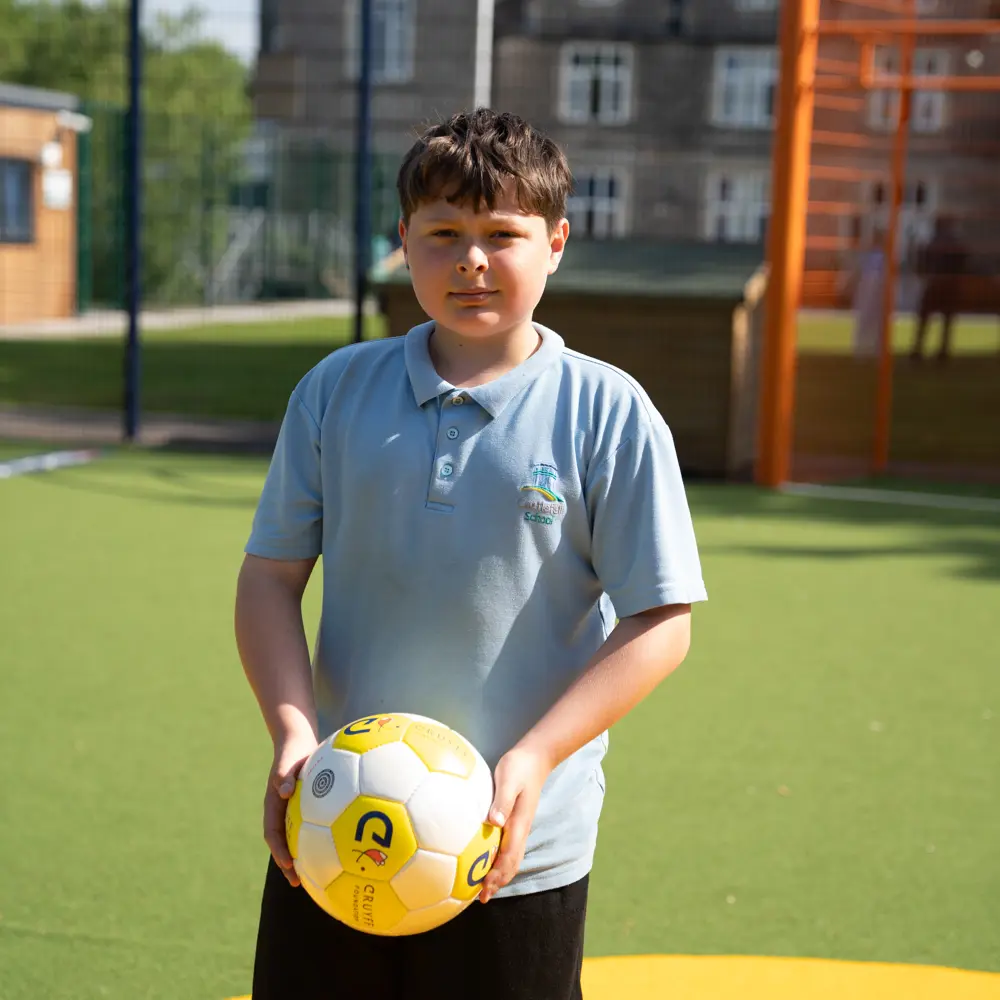 A young boy from Castlefell School on the Cruyff Court holding a football