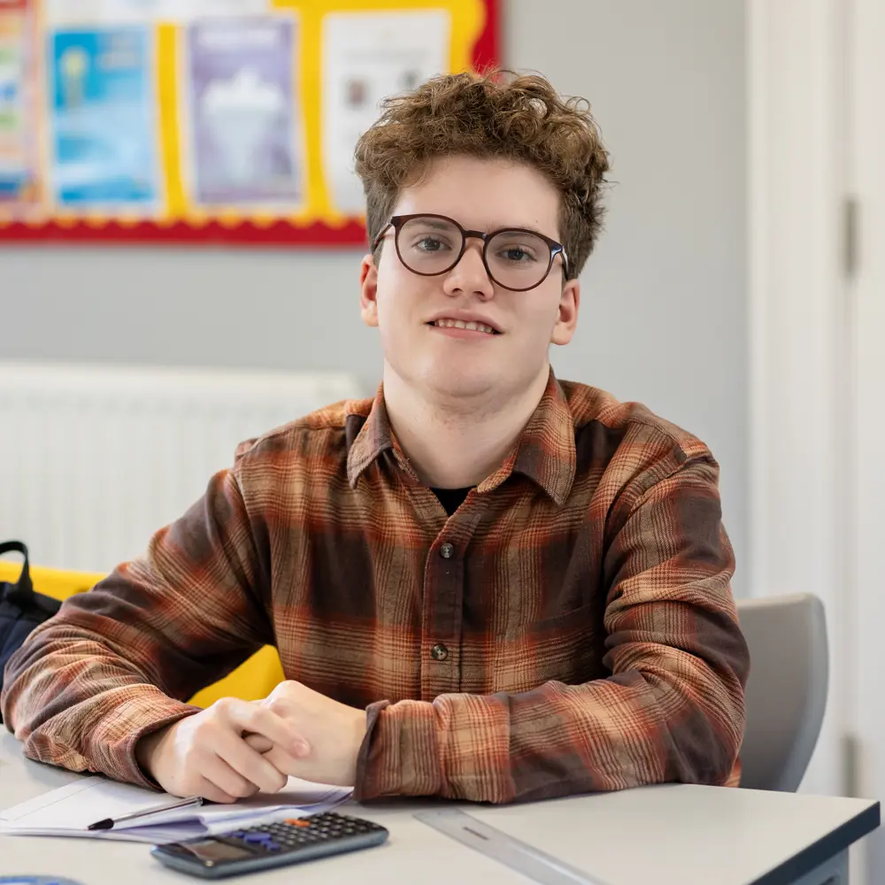 Pupil from Greenholm School wearing a checked shirt sat at a desk engaging in a lesson