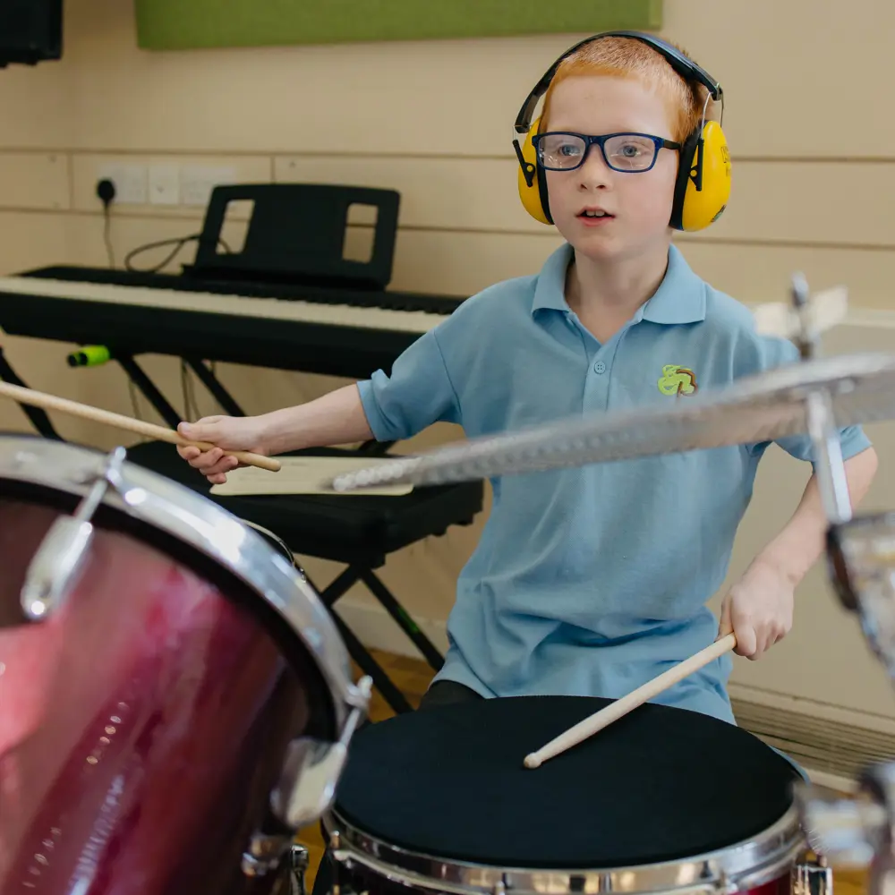 A young boy at Pontville School wearing ear defenders playing the drums
