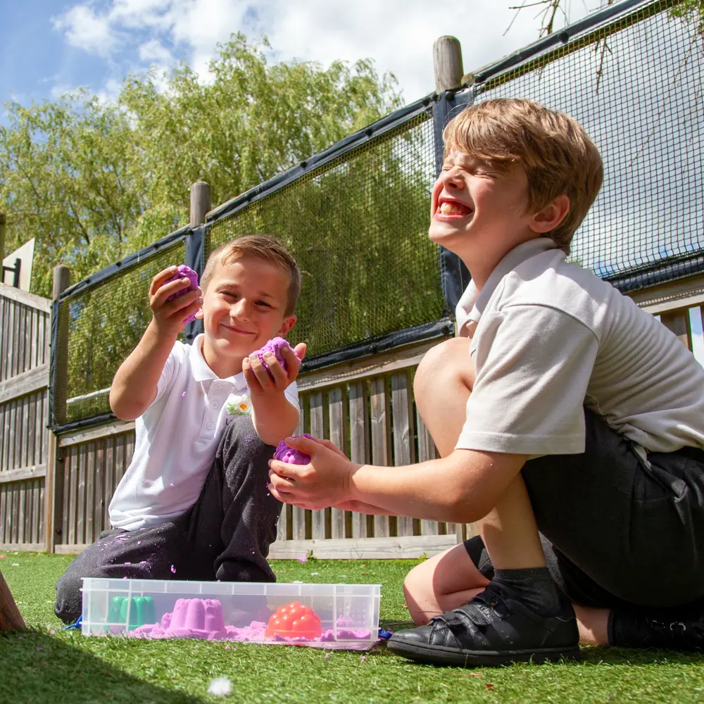 Two young boys from Lakeside School playing wit a sensory box outside smiling